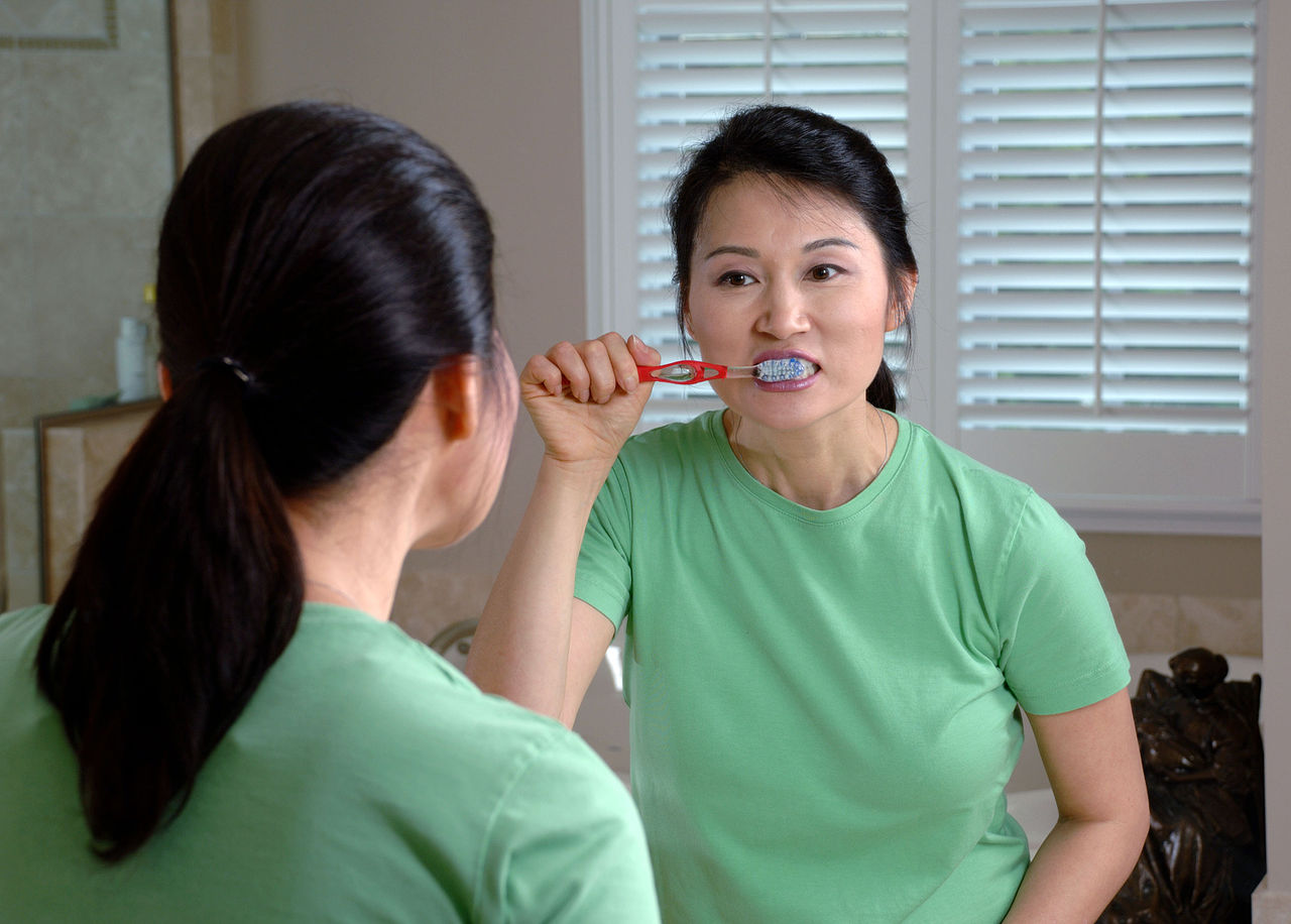 woman brushing teeth in mirror for good oral care