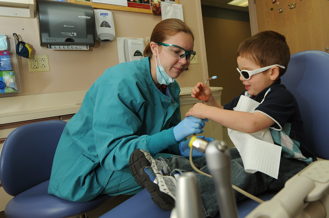 pediatric dentist and young boy in dentist chair looking at a tool