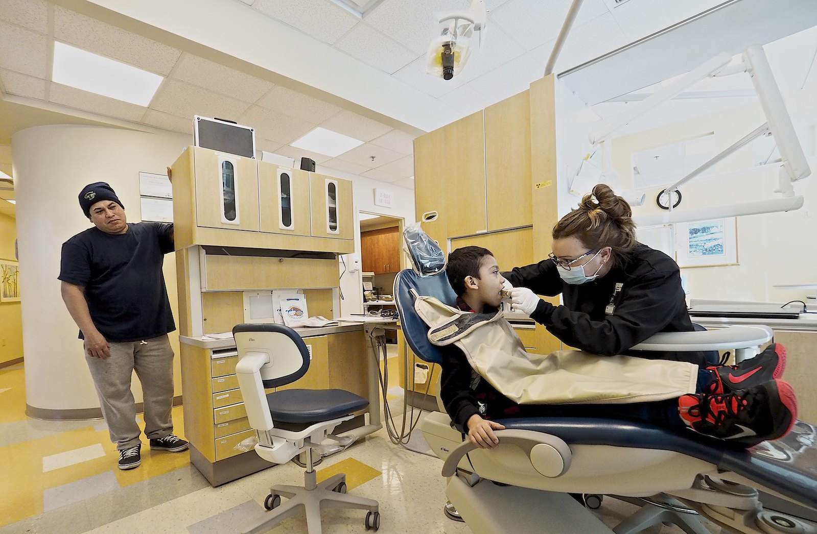 young boy in dentist's chair at dental office while cousin looks on