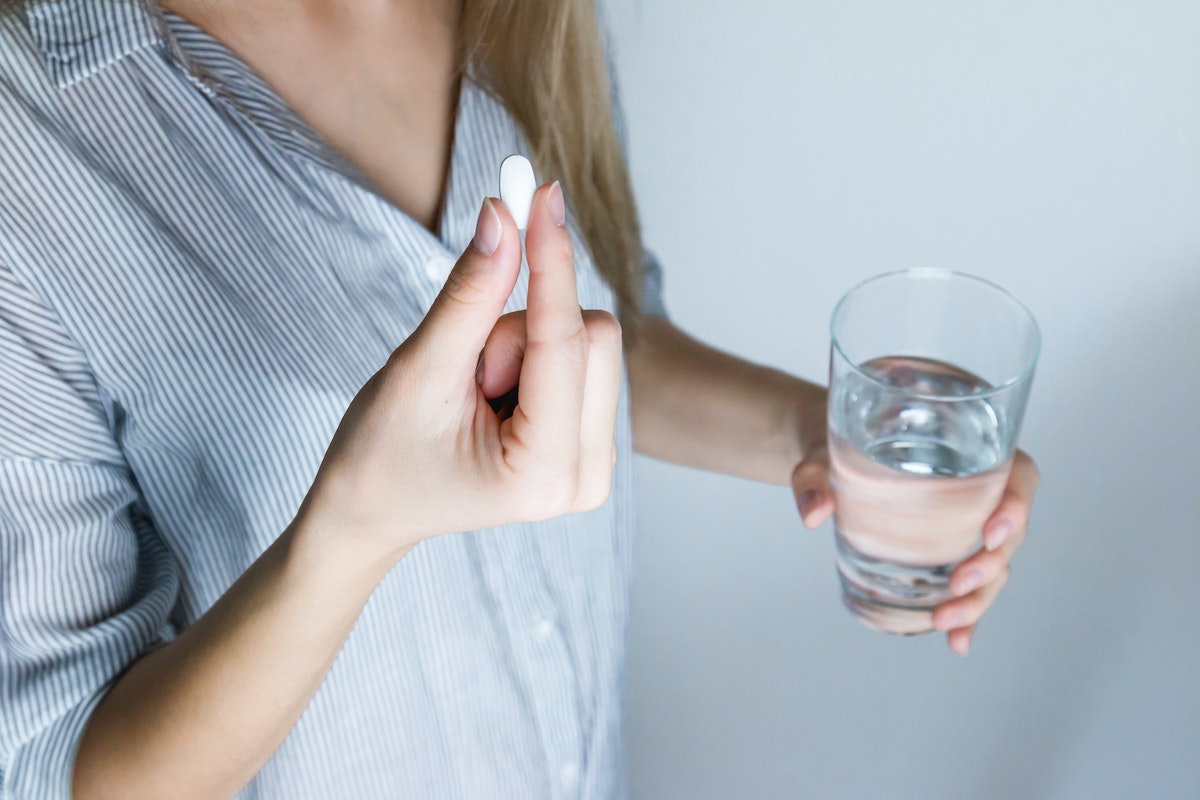 Woman holding a pill and a glass of water, preparing to take pain medication for TMJD pain