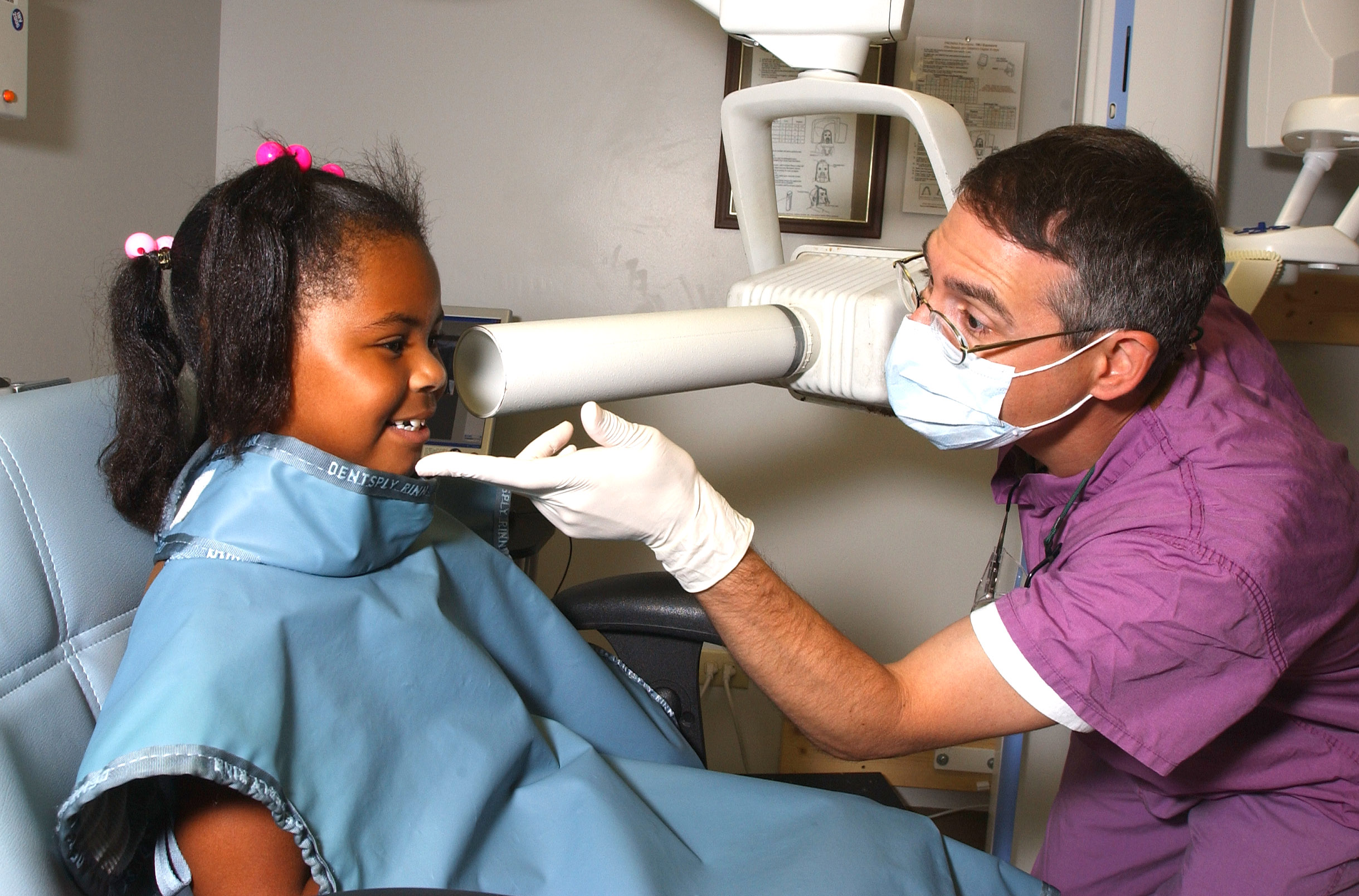 pediatric dentist (kid's dentist) helping a young girl in the dentist's chair